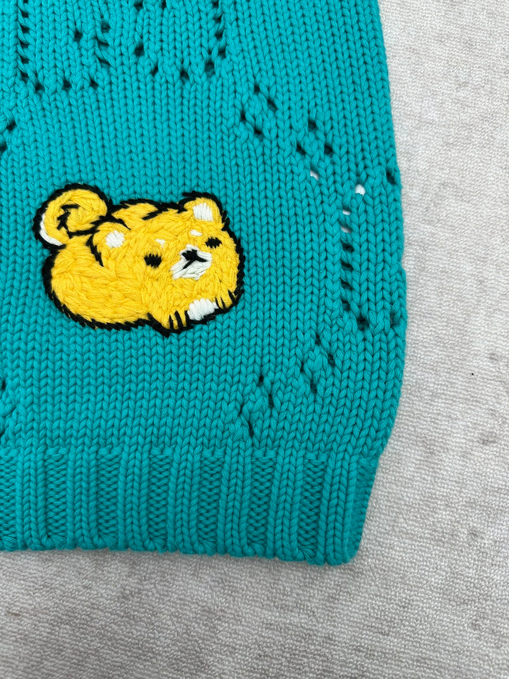 Turquoise knit sweater hem with yellow bear patch
