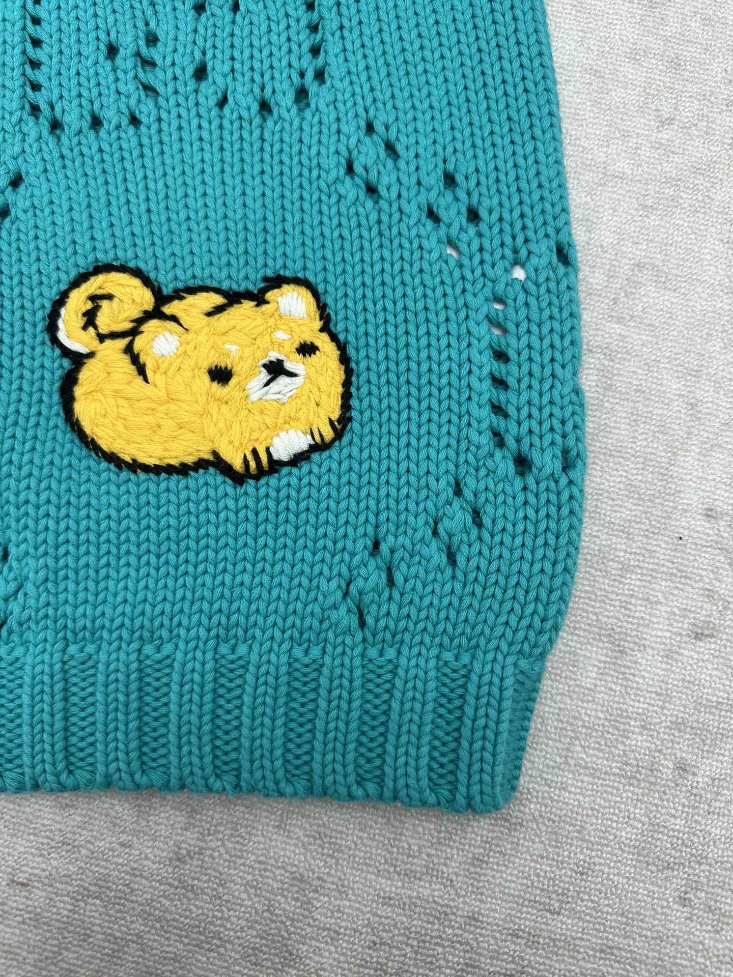 Turquoise knit sweater hem with yellow bear patch