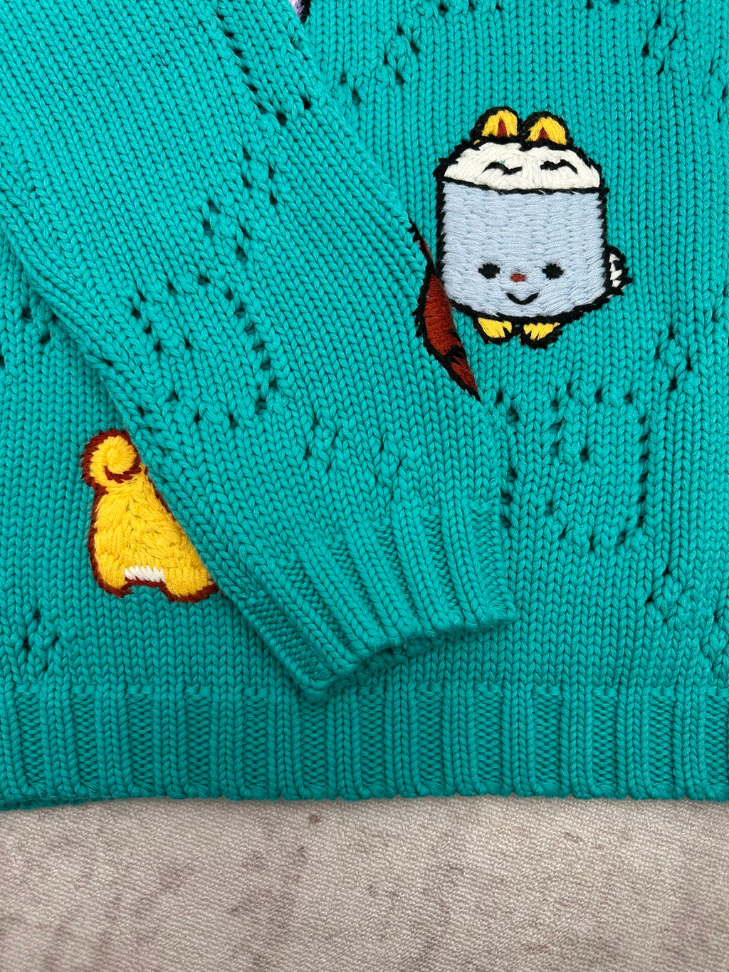 Turquoise knit sweater sleeve cuff with cartoon patch detail and ribbed hem