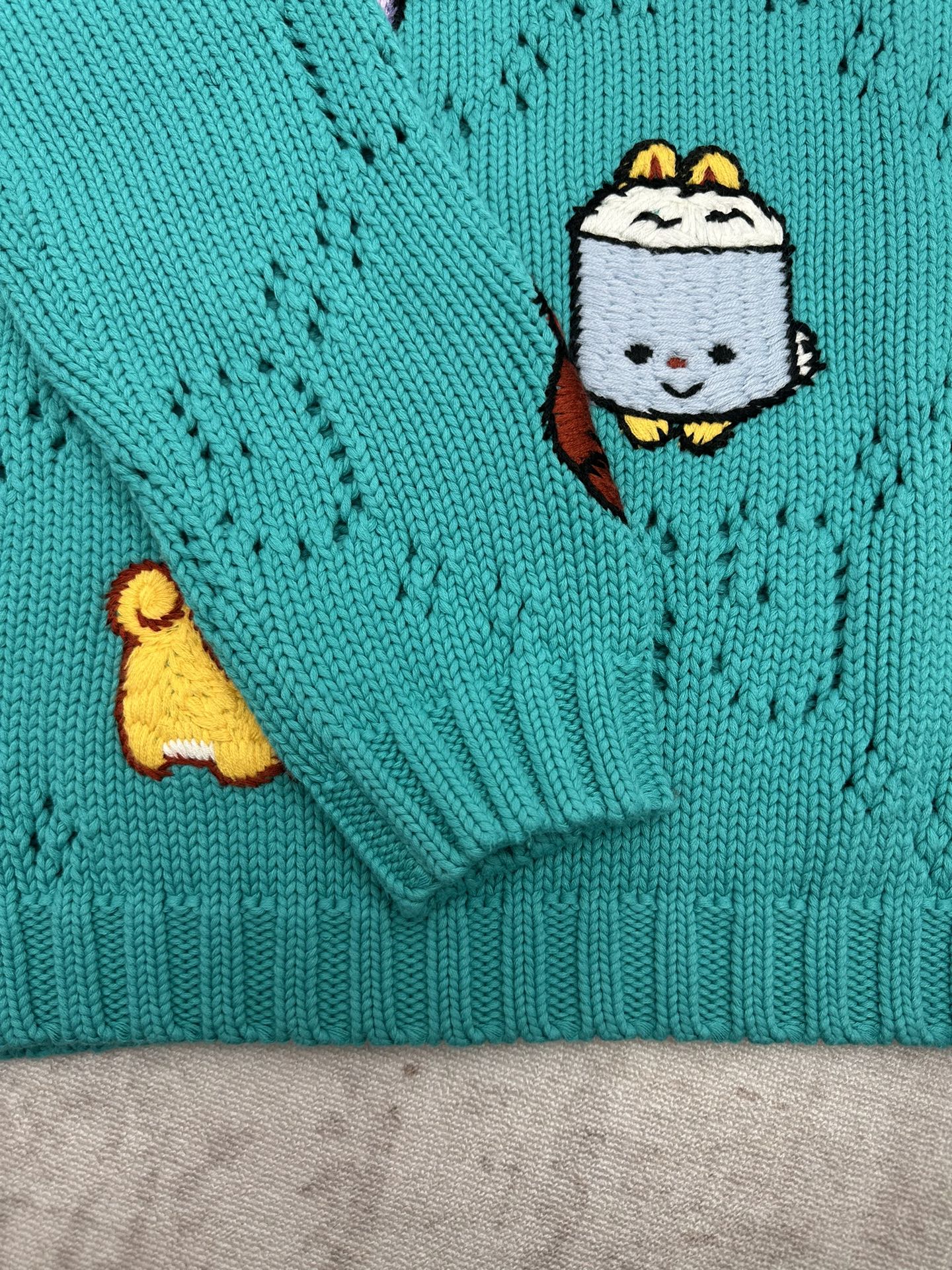 Turquoise knit sweater sleeve cuff with cartoon patch detail and ribbed hem