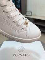 Close-up of white lace-up high-top sneaker with gold hardware and stitched panels.