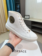 White lace-up high-top sneaker held in hand, with logo patch and gold accents.