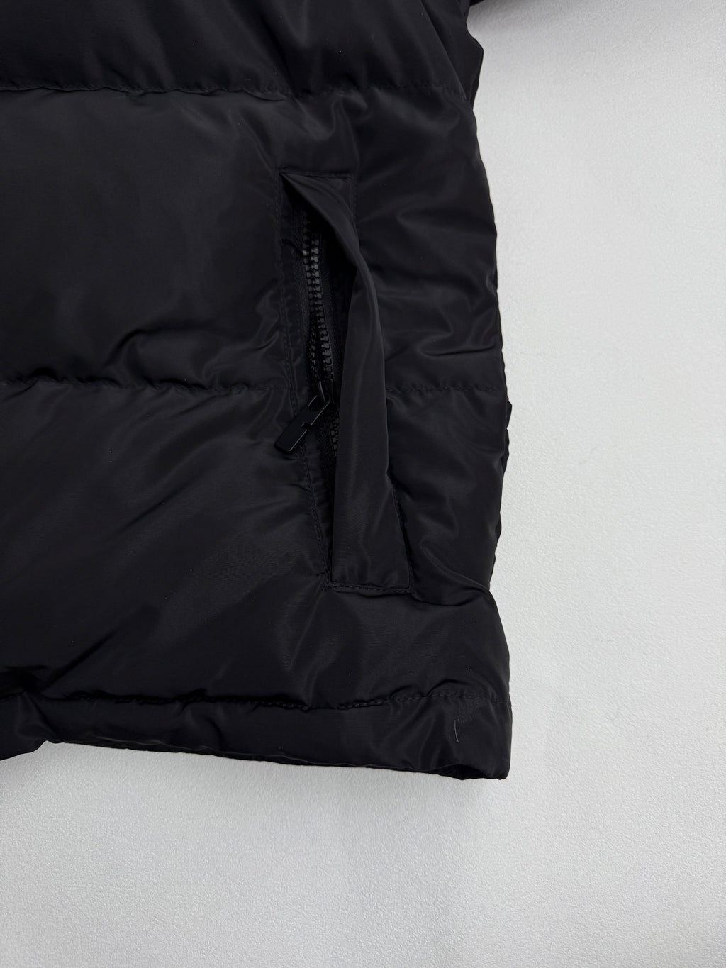 Black puffer jacket side seam with front zipper and quilted hem