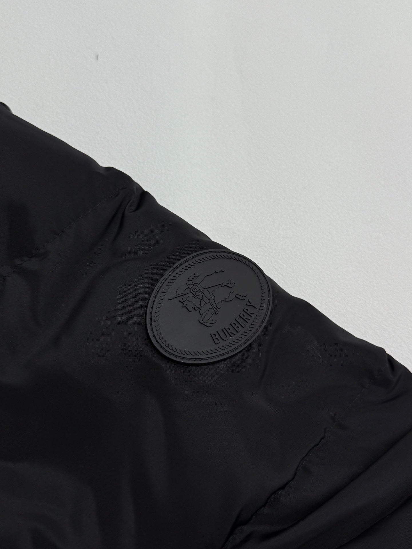 Black jacket shoulder with circular embossed Burberry patch