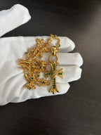 Gold-tone cross pendant necklace with green stone detail, ornate chain on white gloves
