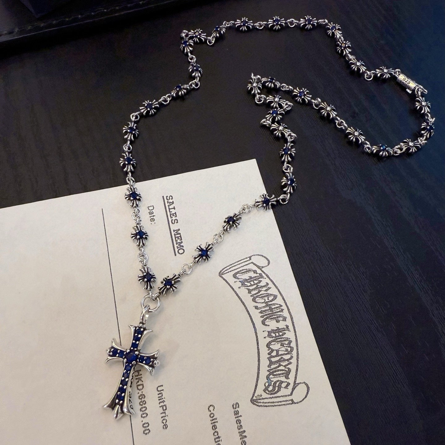 Silver-tone cross pendant necklace with blue inlay, laid out with matching chain.