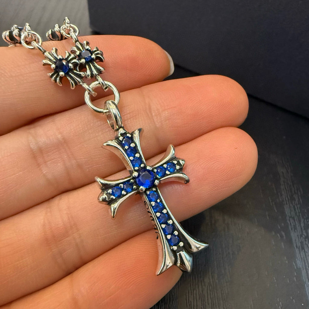 Cross pendant charm with blue inlay on silver-tone chain, close-up on palm.