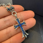 Cross pendant charm with blue inlay on silver-tone chain, close-up on palm.