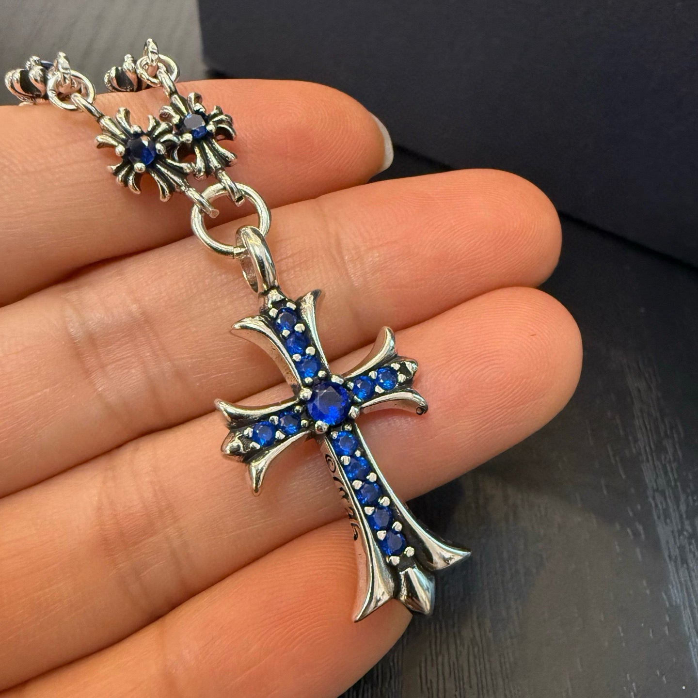 Cross pendant charm with blue inlay on silver-tone chain, close-up on palm.