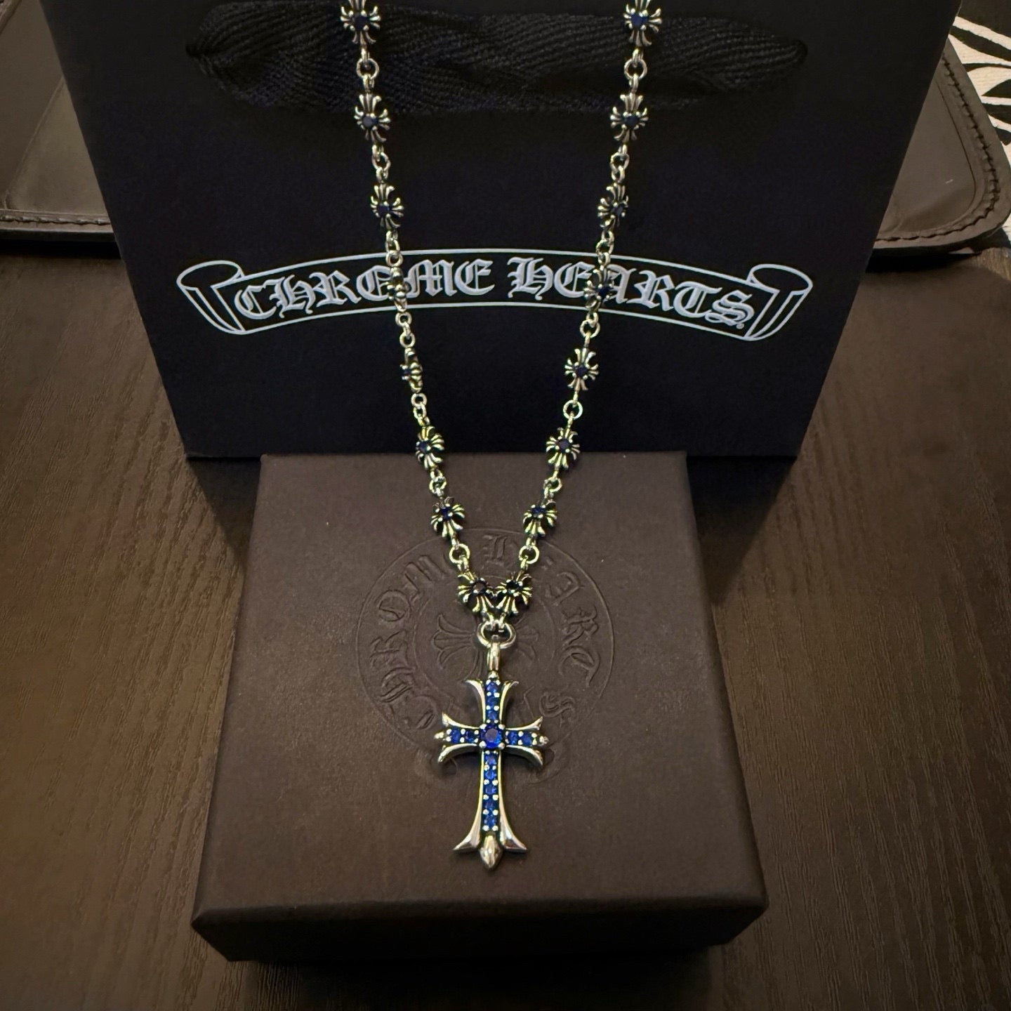 Silver-tone cross pendant necklace with blue inlay, on a black display stand.