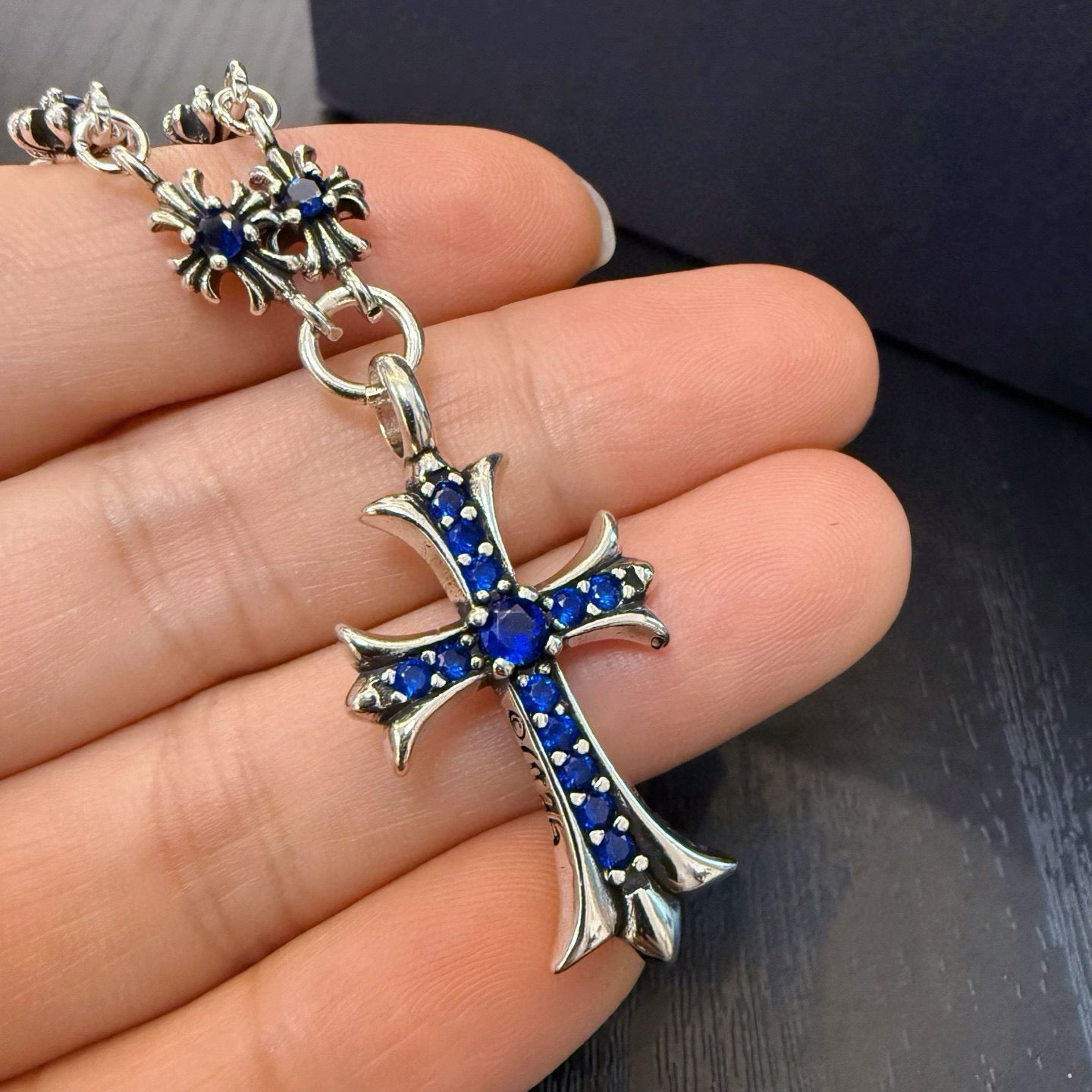 Cross pendant charm with blue inlay on a silver-tone chain, close-up on hand.