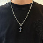 Cross pendant necklace worn on a black shirt; silver-tone chain with blue inlay cross.