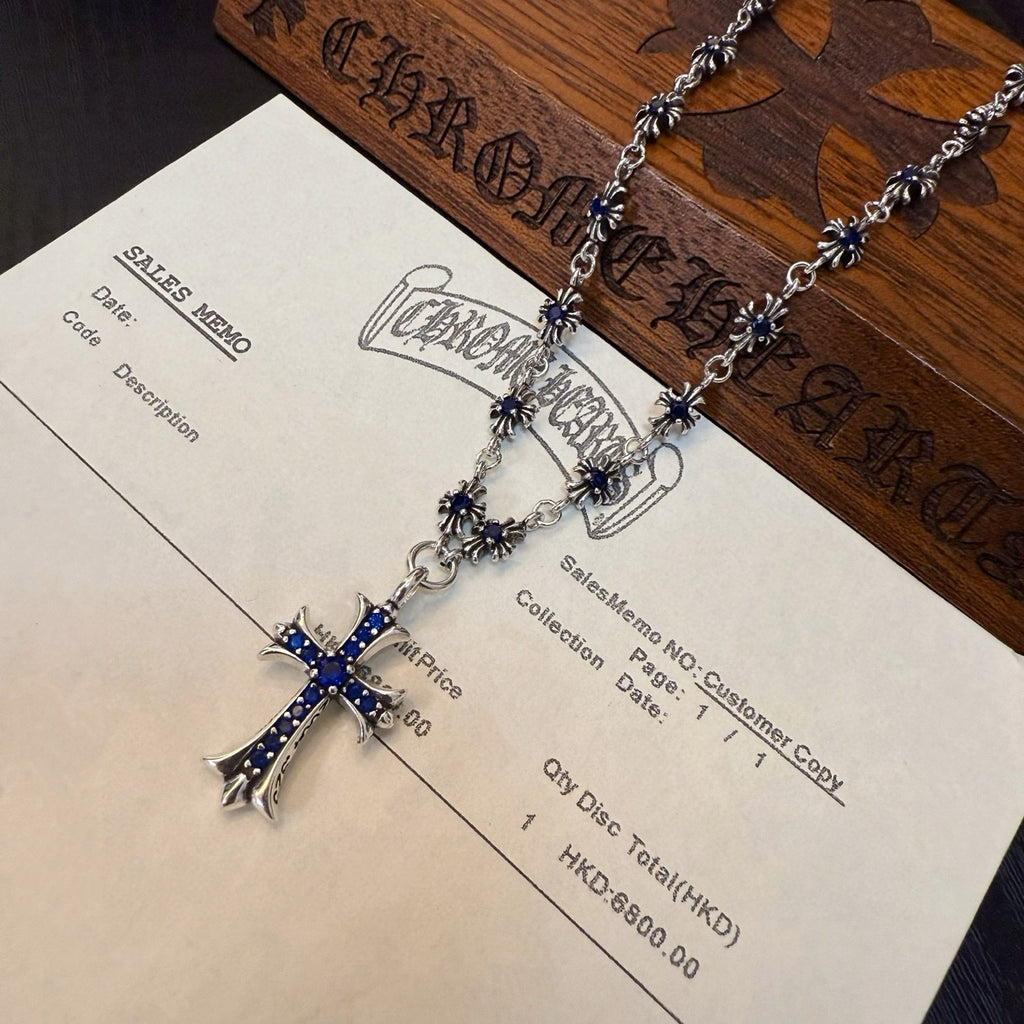 Silver-tone cross pendant necklace with blue inlay, laid on a product label card.