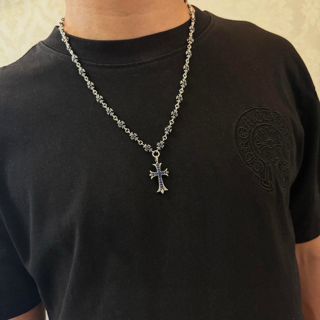 Cross pendant necklace worn on a black shirt; silver-tone chain with blue inlay cross.