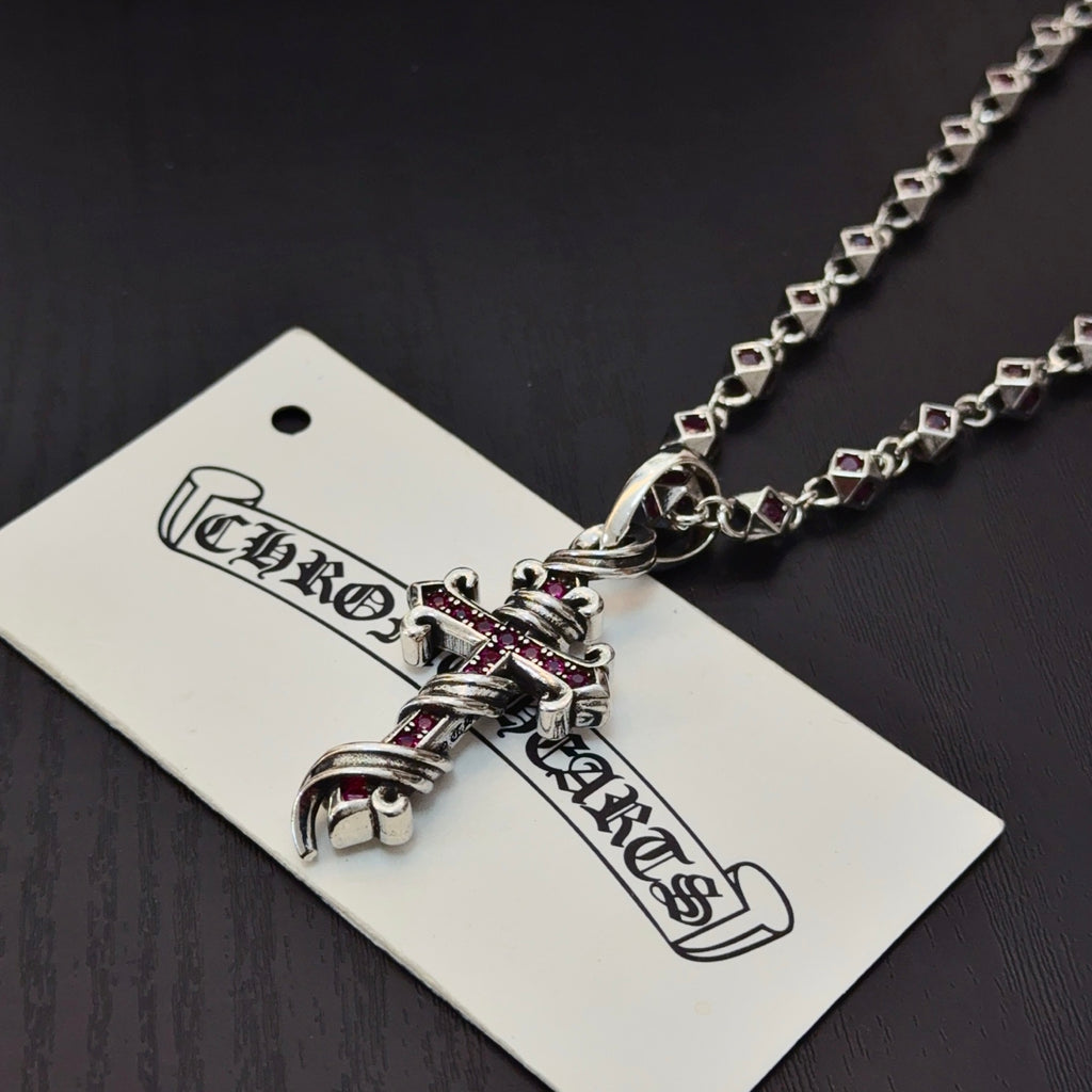 Cross pendant necklace with silver links and pink enamel accents, close-up