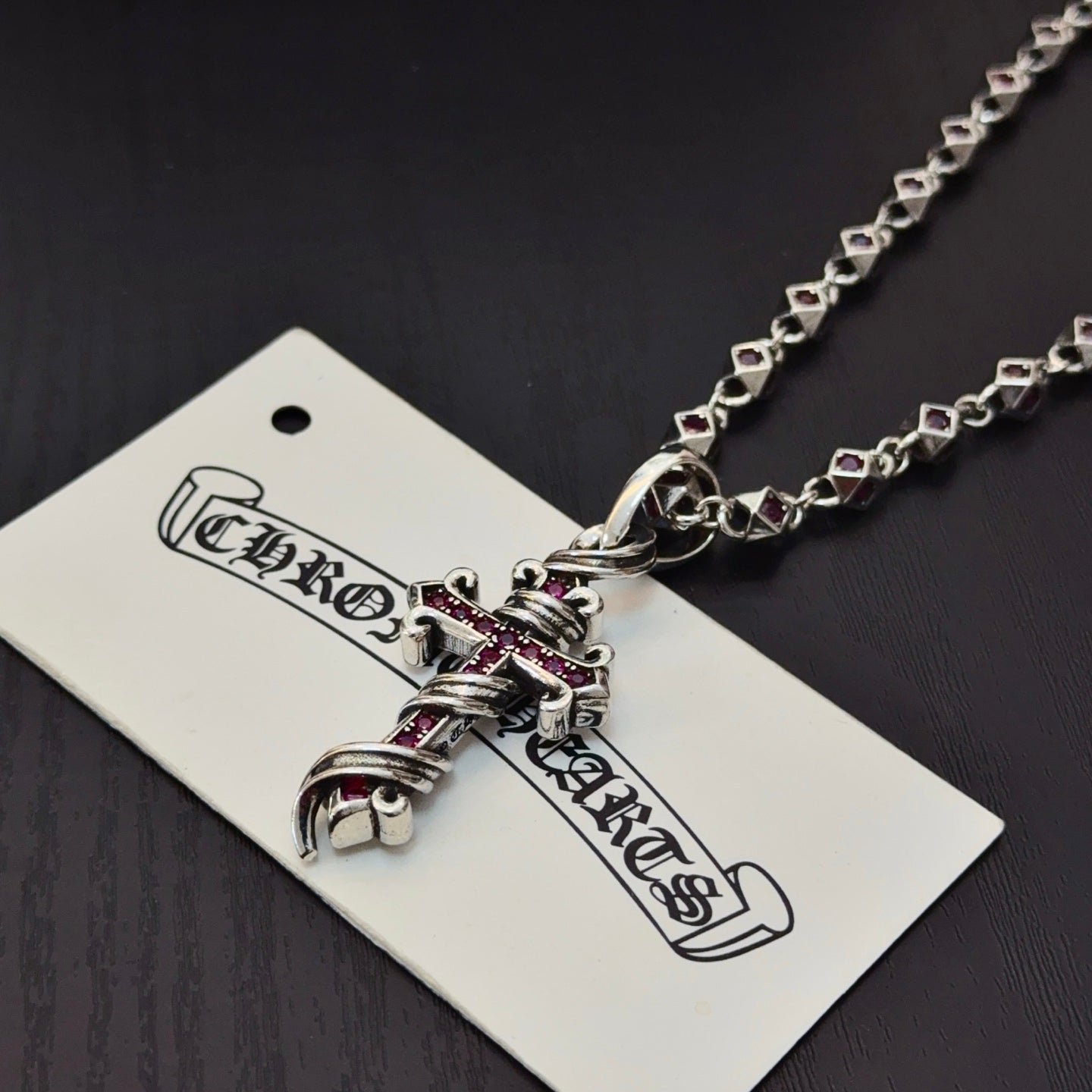 Cross pendant necklace with silver links and pink enamel accents, close-up