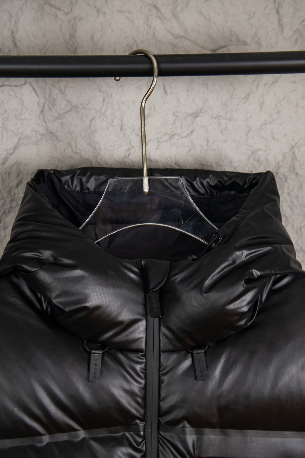 Hooded long puffer jacket hanging on rack, dark with front zip and sleeve tags