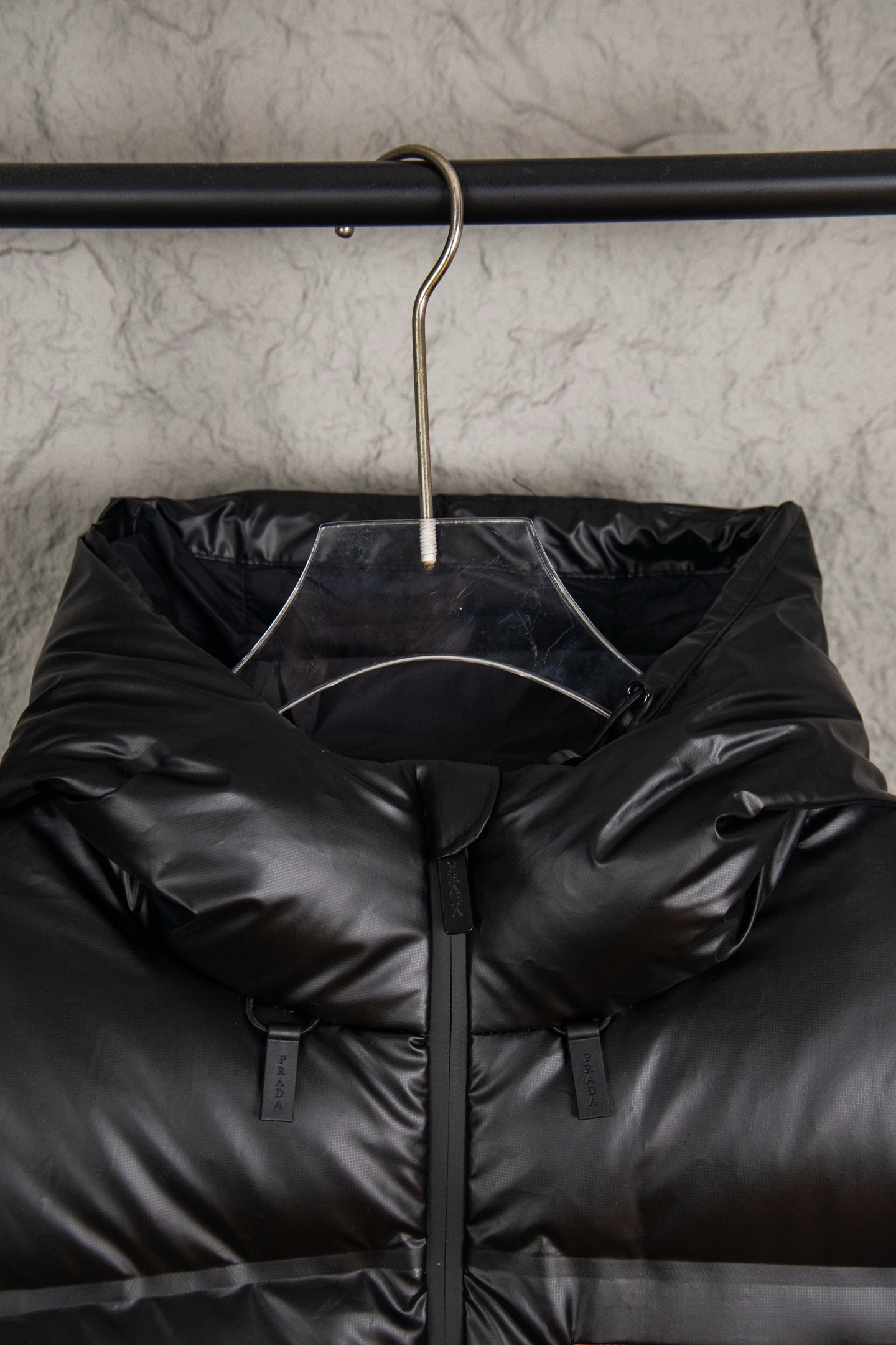 Hooded long puffer jacket hanging on rack, dark with front zip and sleeve tags