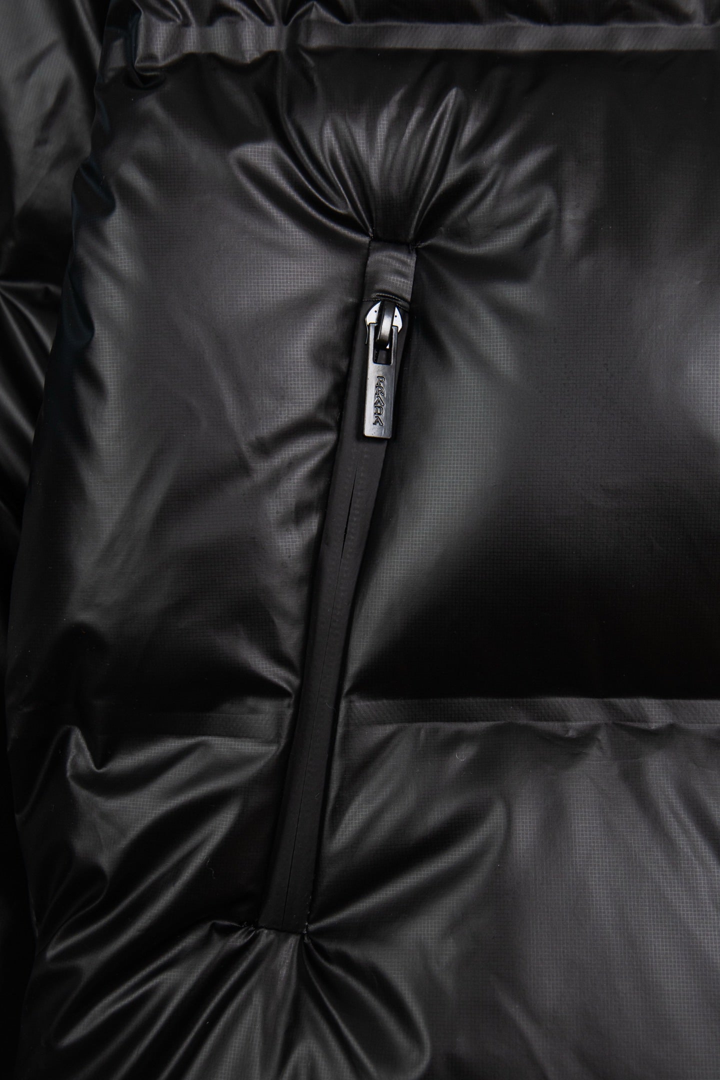 Front detail of dark puffer jacket zipper with quilted, puffed panels