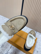 Beige slip-on shoes with white shearling trim, gold emblem, and dark rubber edge