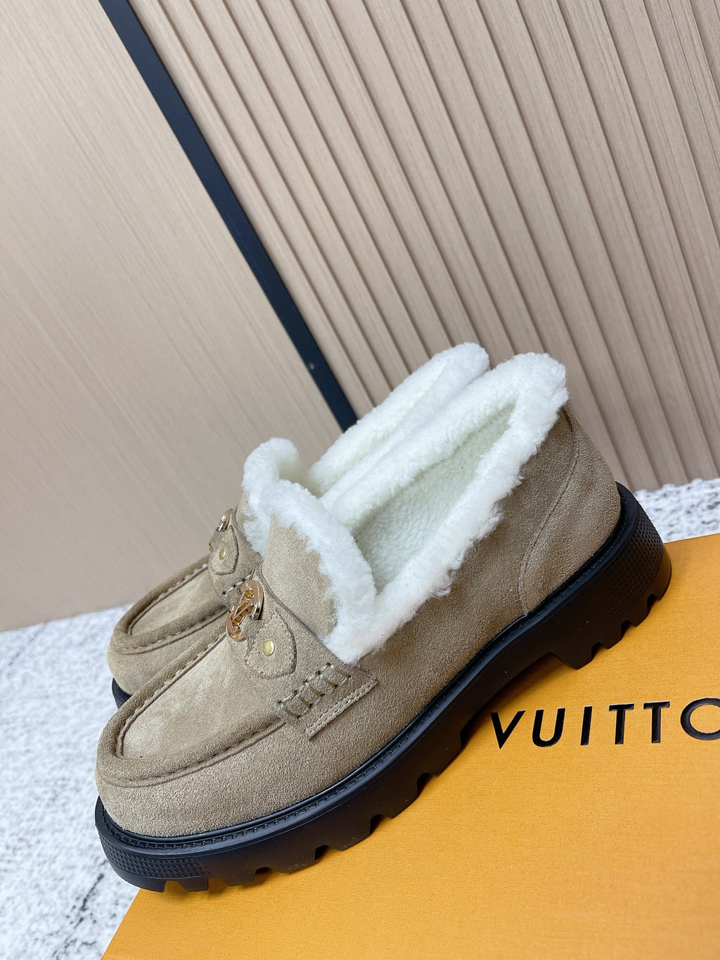 Beige suede loafer-style shoes with white shearling lining and gold logo hardware