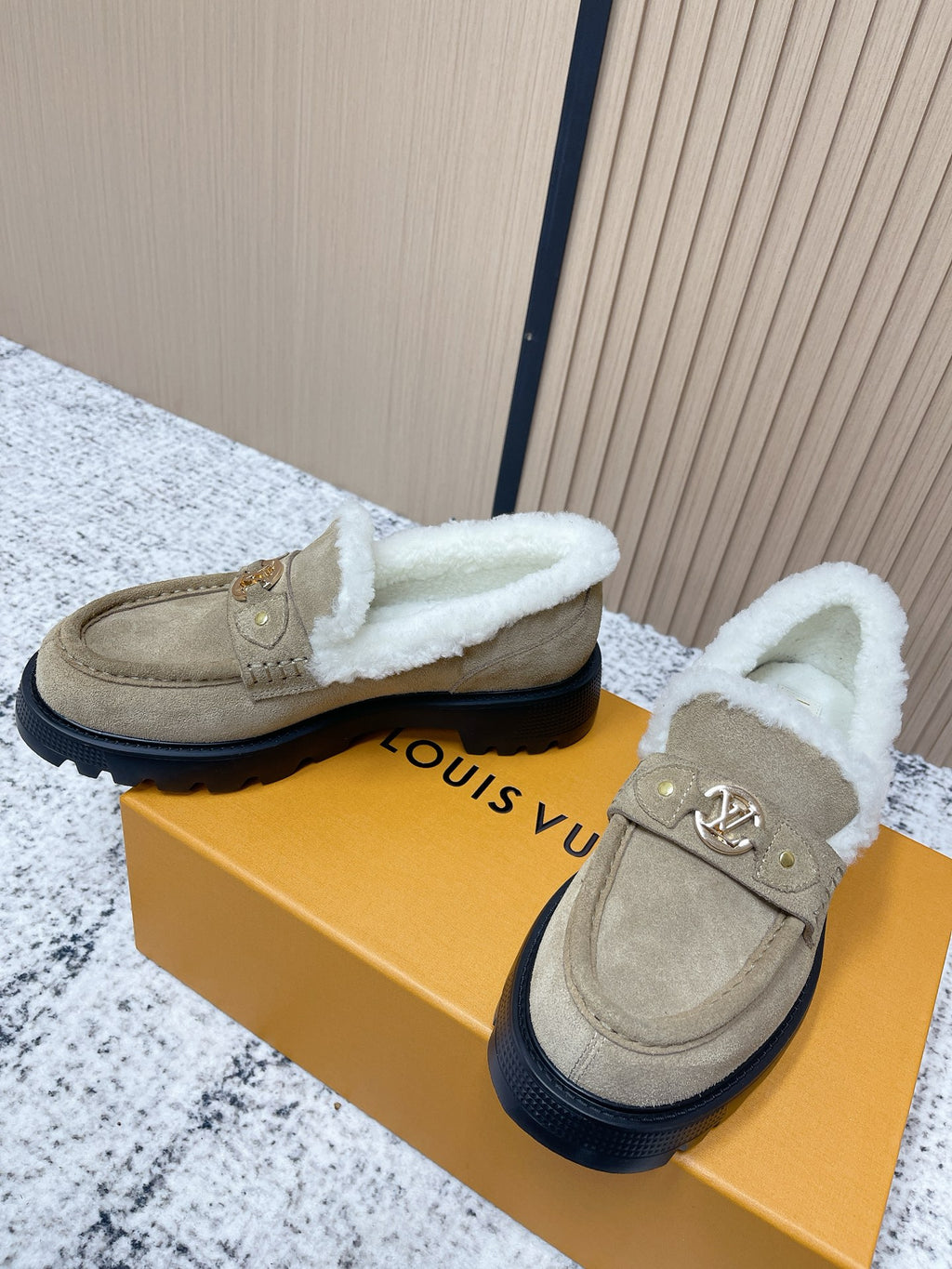 Pair of beige suede slip-on shoes with plush white trim and dark tread sole