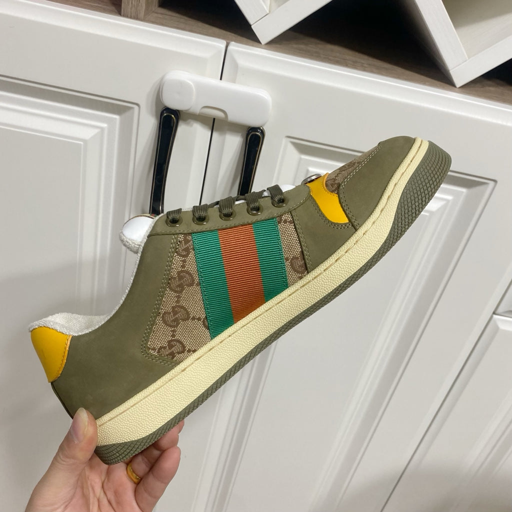 Low-top unisex sneakers in olive canvas with GG panel, orange-green stripe, held up for view