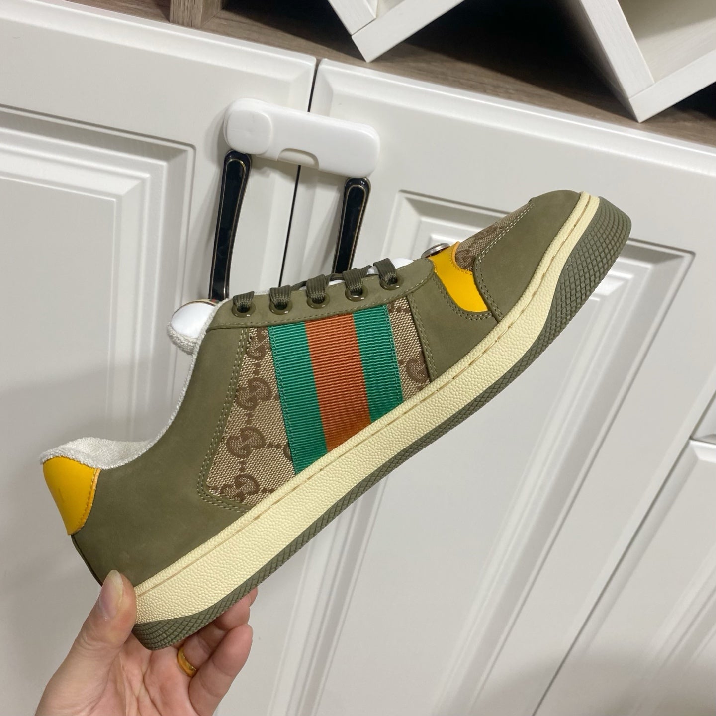 Low-top unisex sneakers in olive canvas with GG panel, orange-green stripe, held up for view