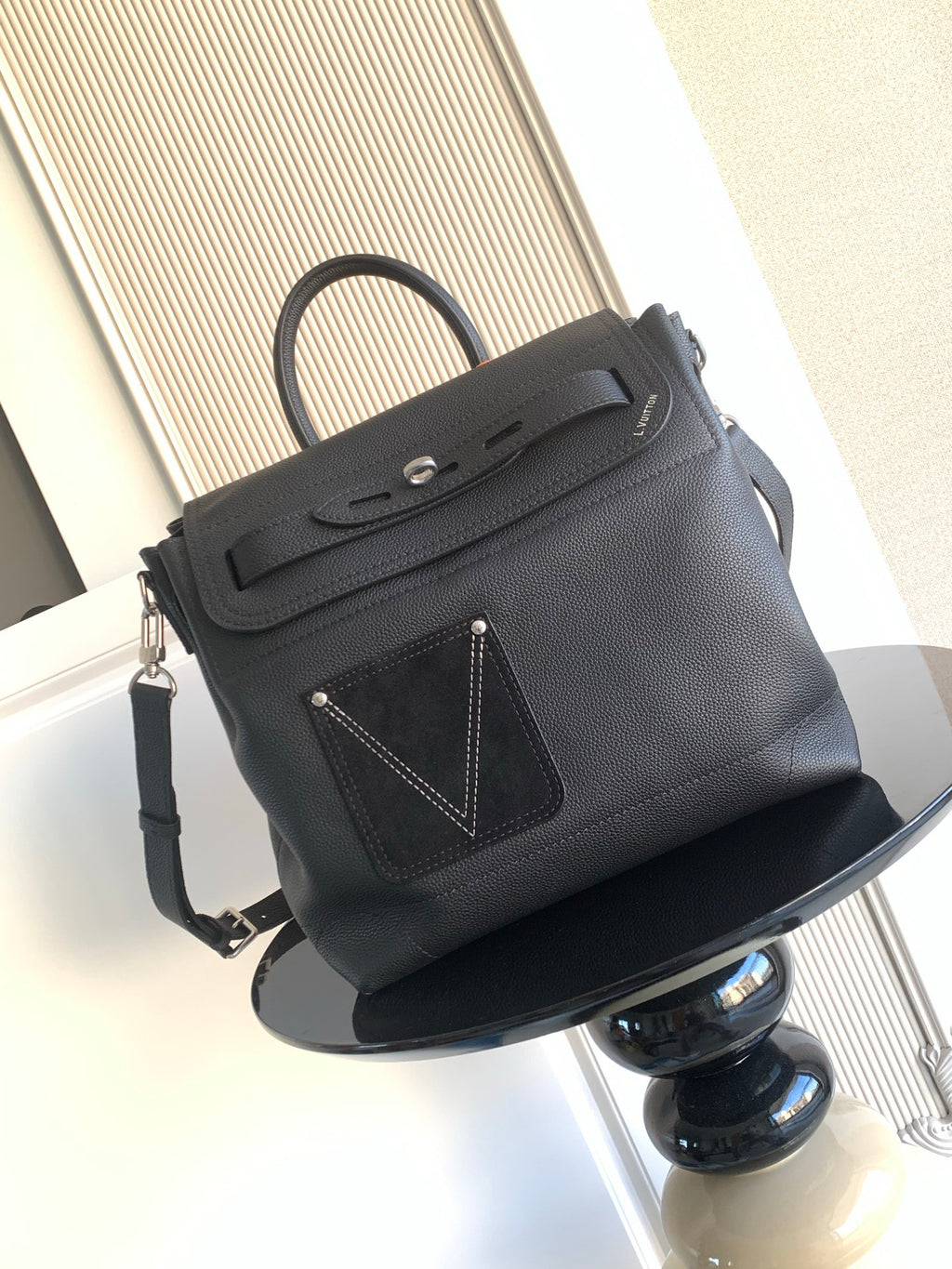 Men’s black leather top-handle bag with flap, strap, and front stitched emblem