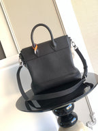 Black leather handbag with top handle and shoulder strap, angled view