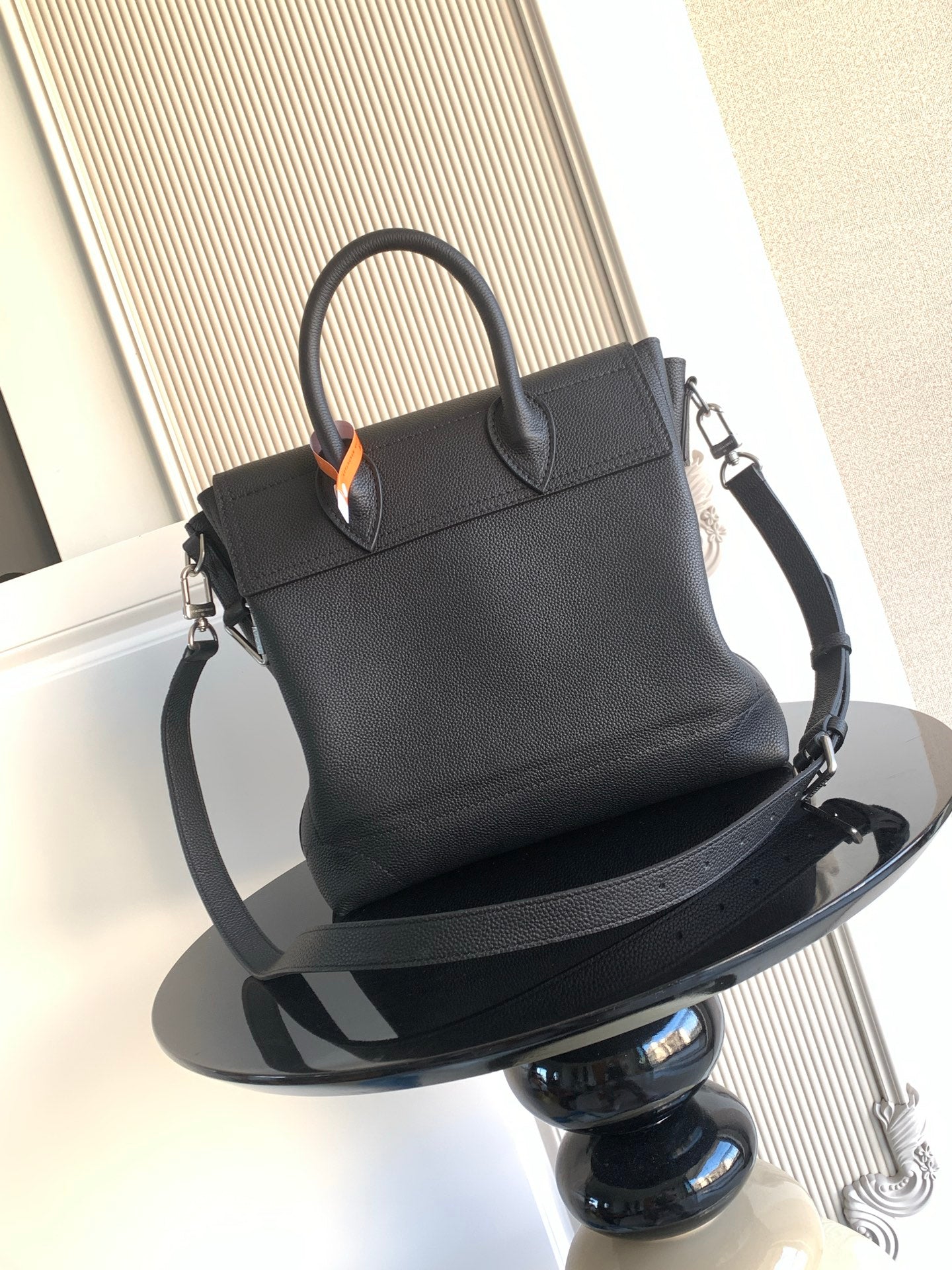 Black leather handbag with top handle and shoulder strap, angled view