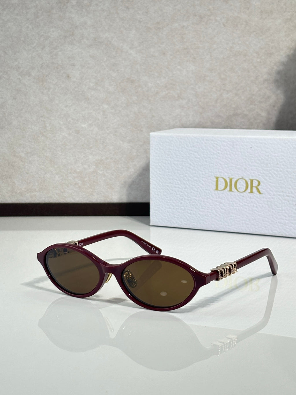 Dior sunglasses with burgundy frame and oval lenses, gold bridge detail.