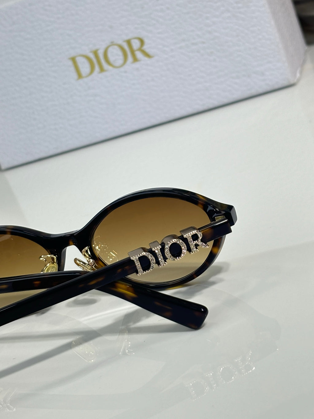 Dior sunglasses close-up: black temple with gold logo, oval lens edge visible.