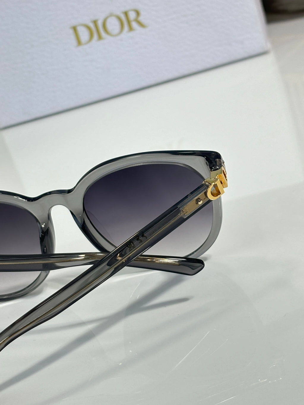 Sunglasses side view with dark frame, gold logo detail, and dark gradient lenses