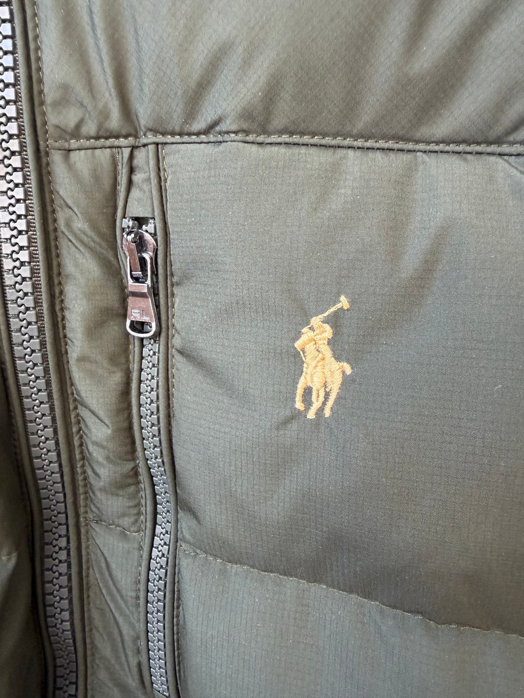 Olive puffer jacket close-up with silver zipper and small yellow polo logo