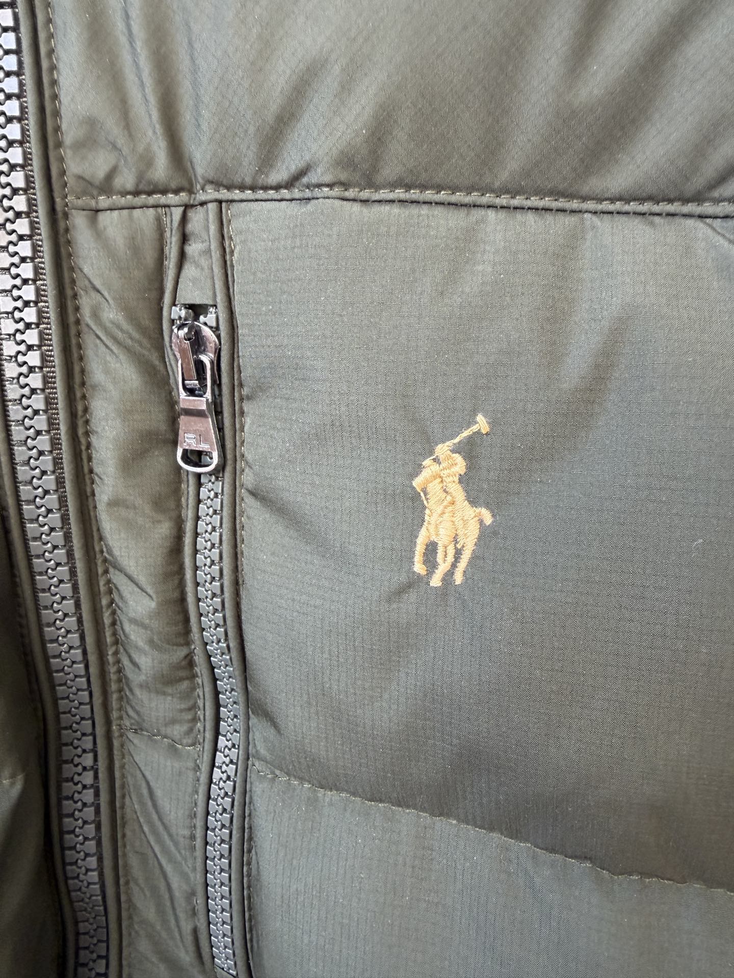 Olive puffer jacket close-up with silver zipper and small yellow polo logo