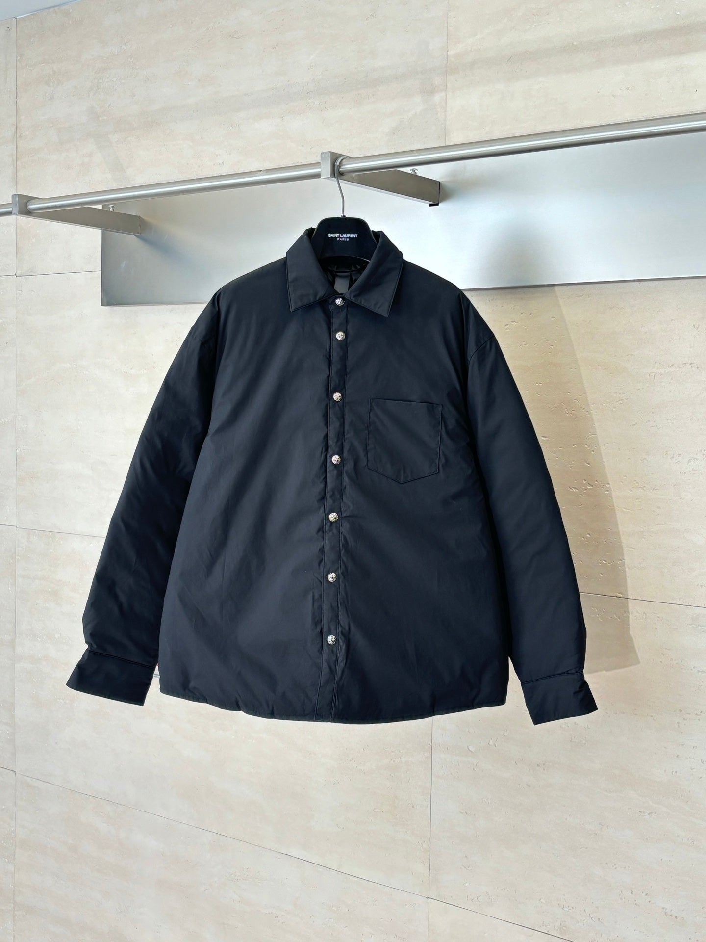 Long-sleeve black button-up jacket with collar and chest pocket, hanging on a rail