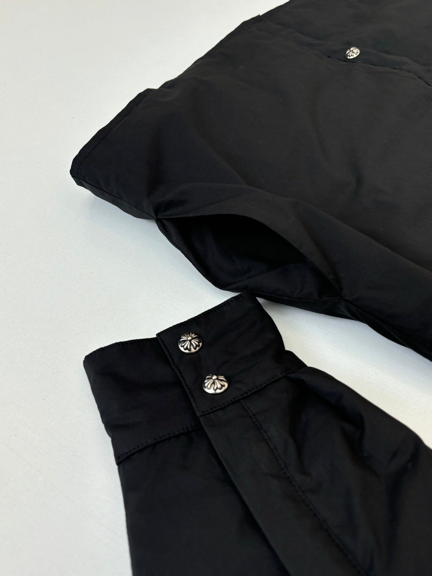 Black long-sleeve jacket pieces shown on a flat surface with decorative buttons