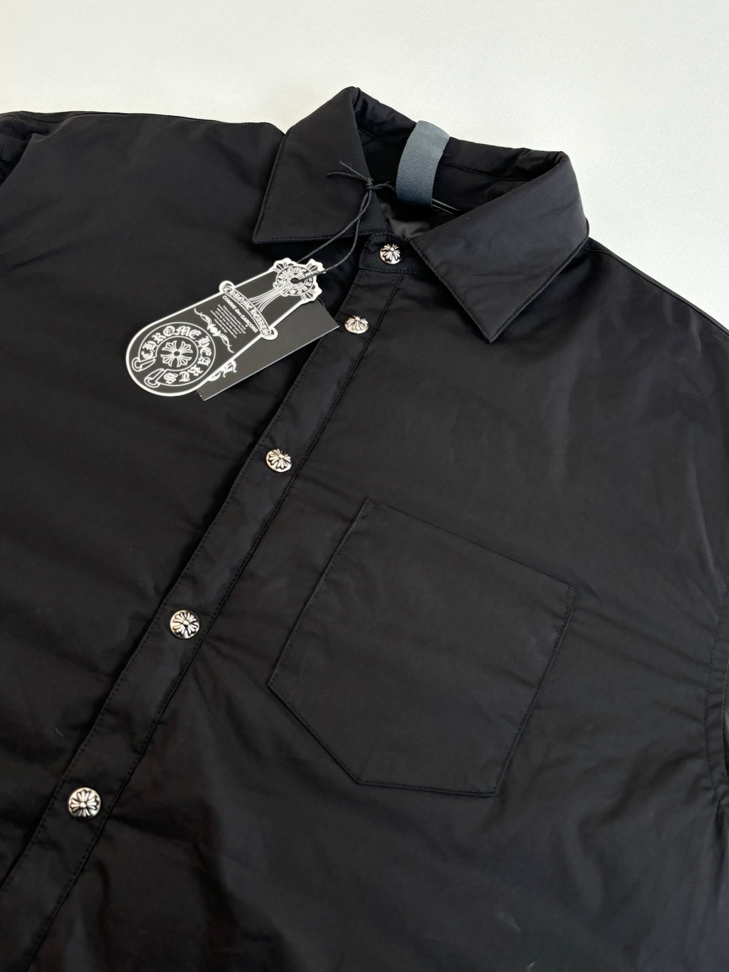 Close-up of black long-sleeve button-up jacket with decorative buttons and chest pocket