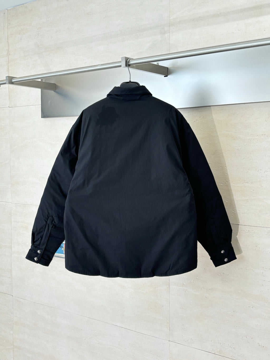 Back view of black long-sleeve button-up jacket with stand collar, hanging on a rail