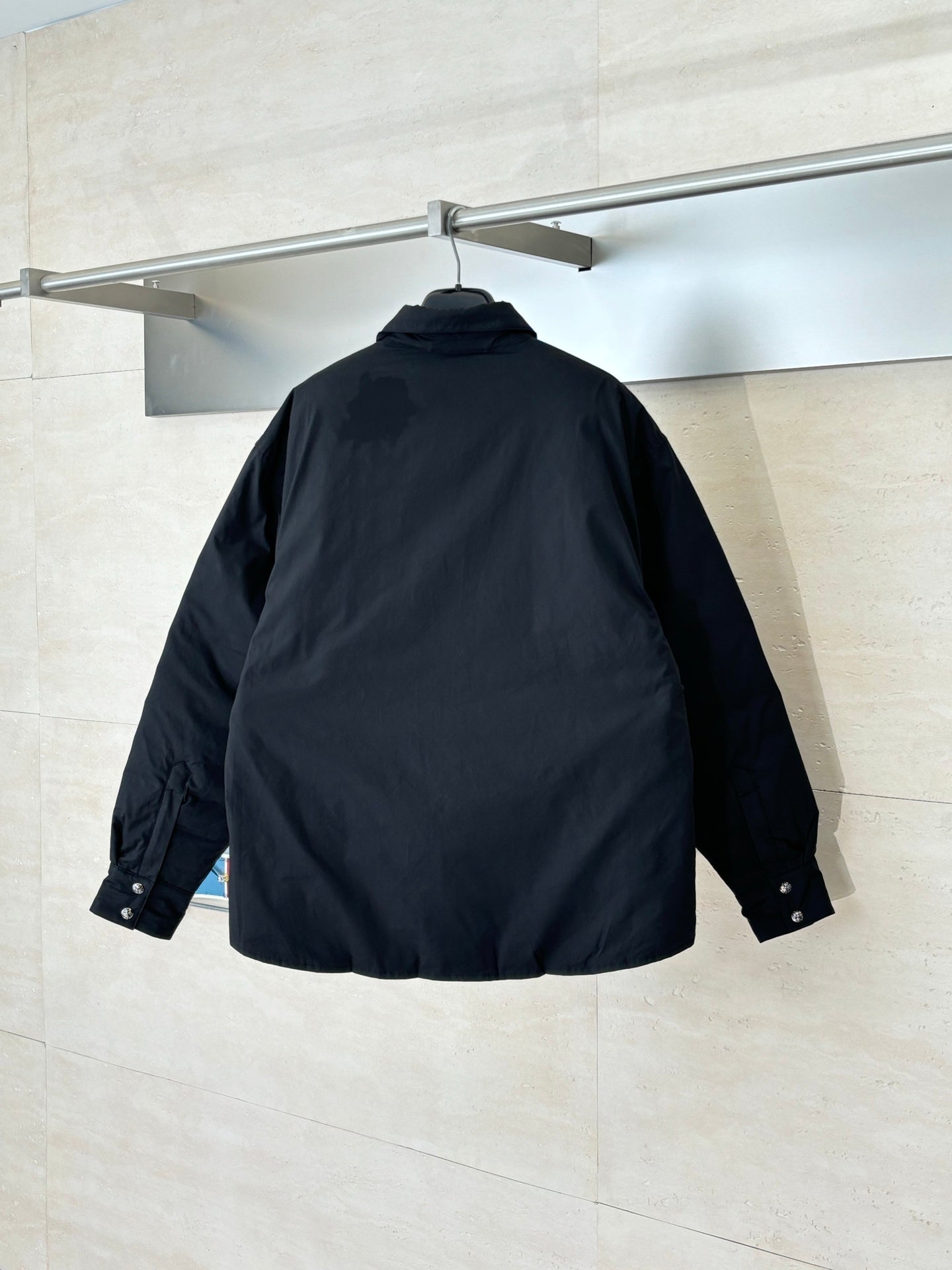 Back view of black long-sleeve button-up jacket with stand collar, hanging on a rail