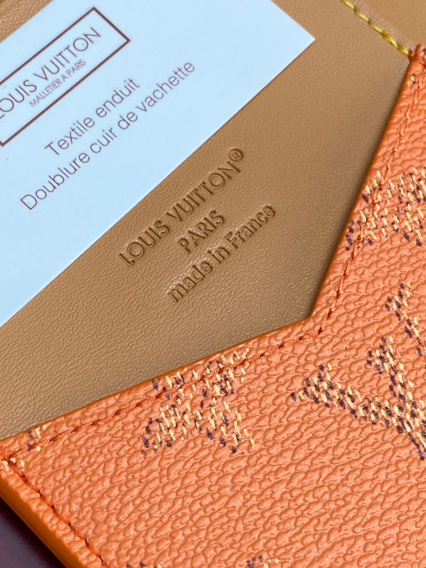 Small Louis Vuitton bag close-up showing embossed logo on tan leather