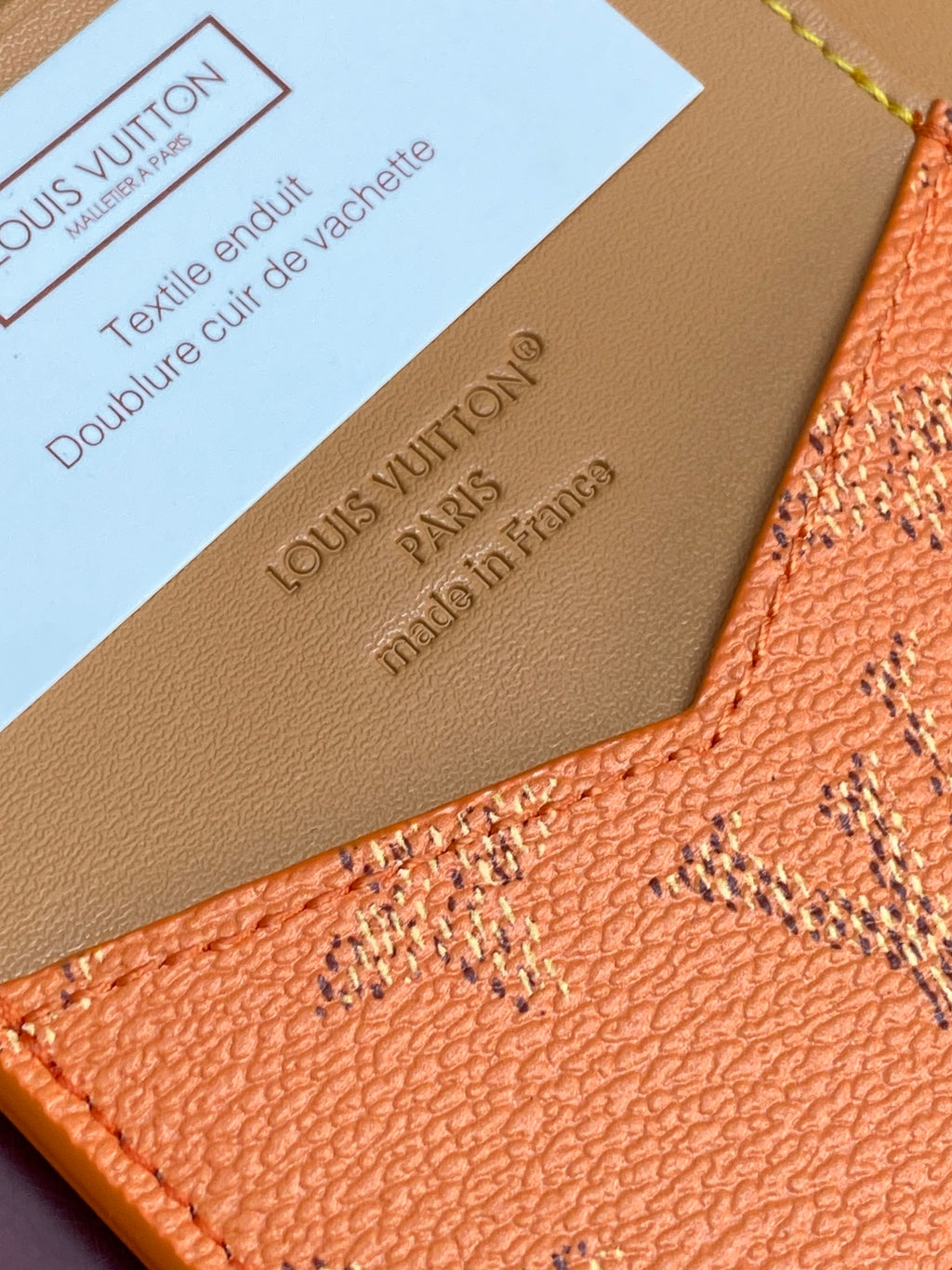 Louis Vuitton leather cardholder corner close-up with embossed text and orange monogram