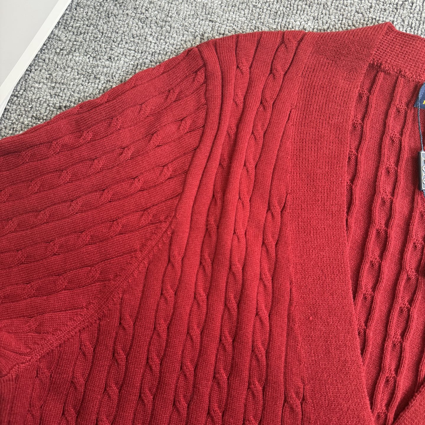 Red cable-knit cardigan fabric close-up with textured vertical cable pattern