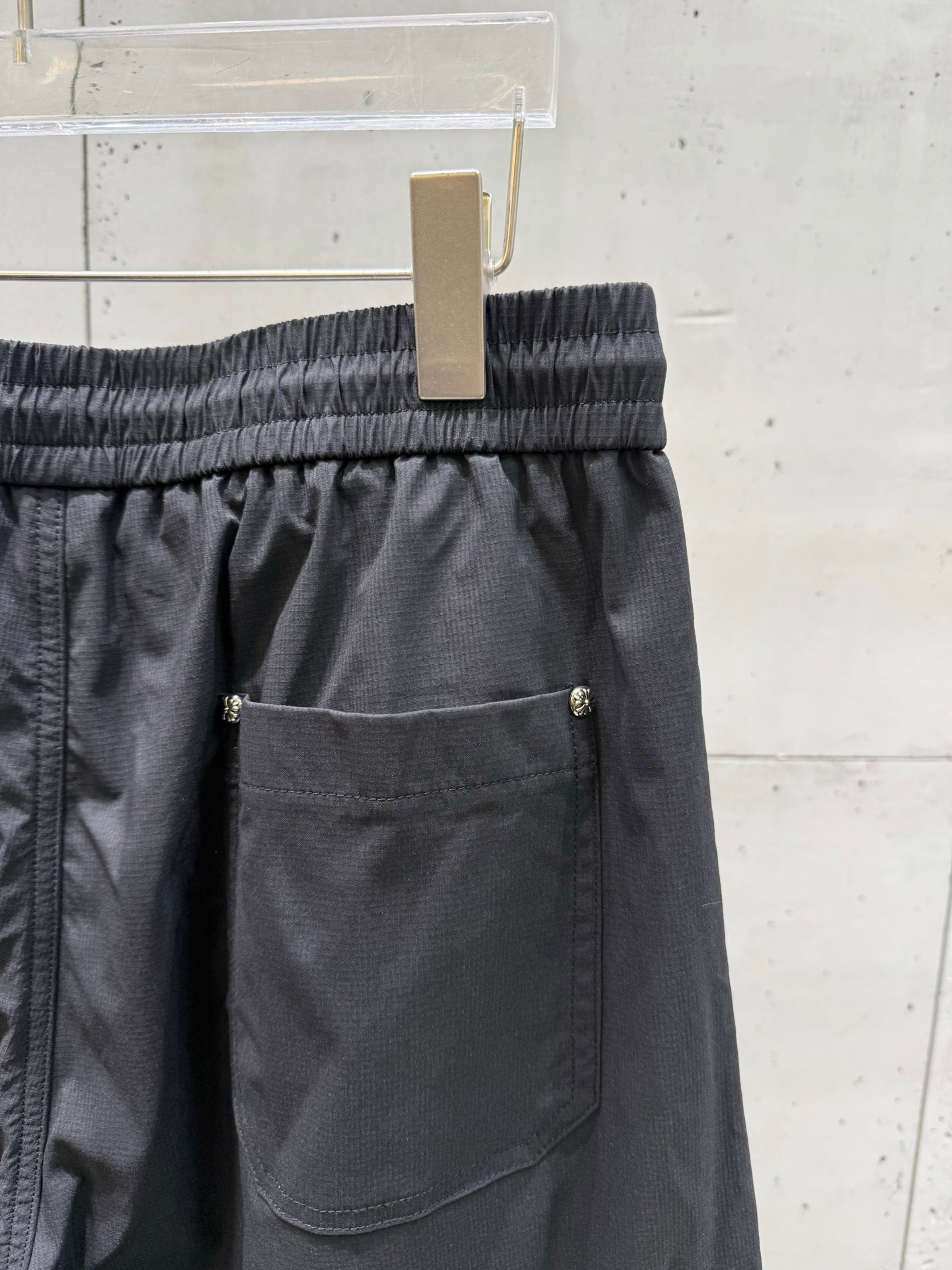 Chrome pants front pocket with button closure, elastic waistband, dark fabric.