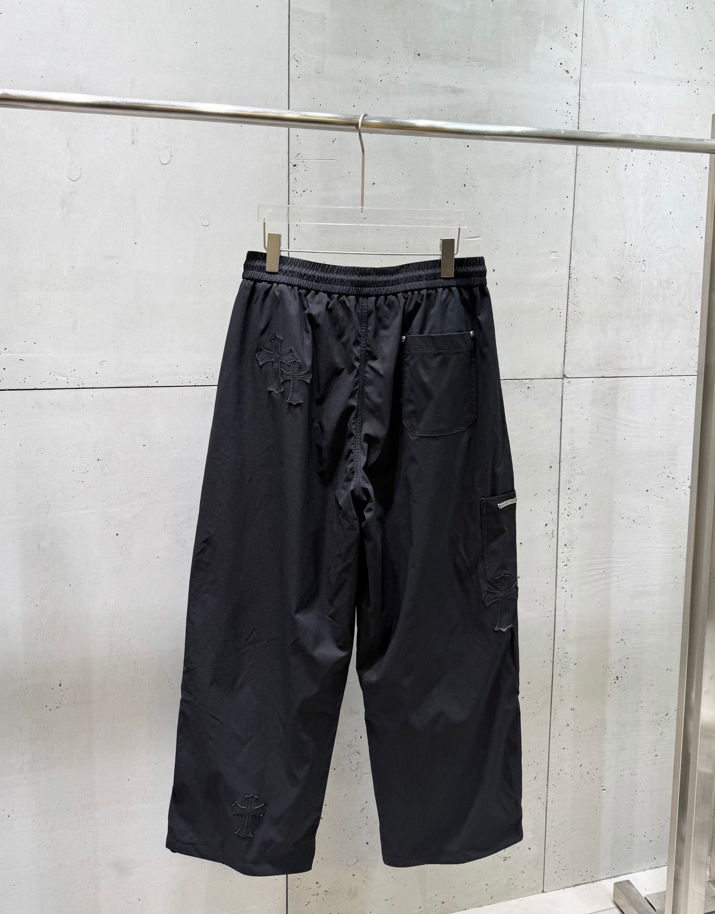 Chrome pants hanging view, elastic waistband, dark wide-leg silhouette with side pockets.