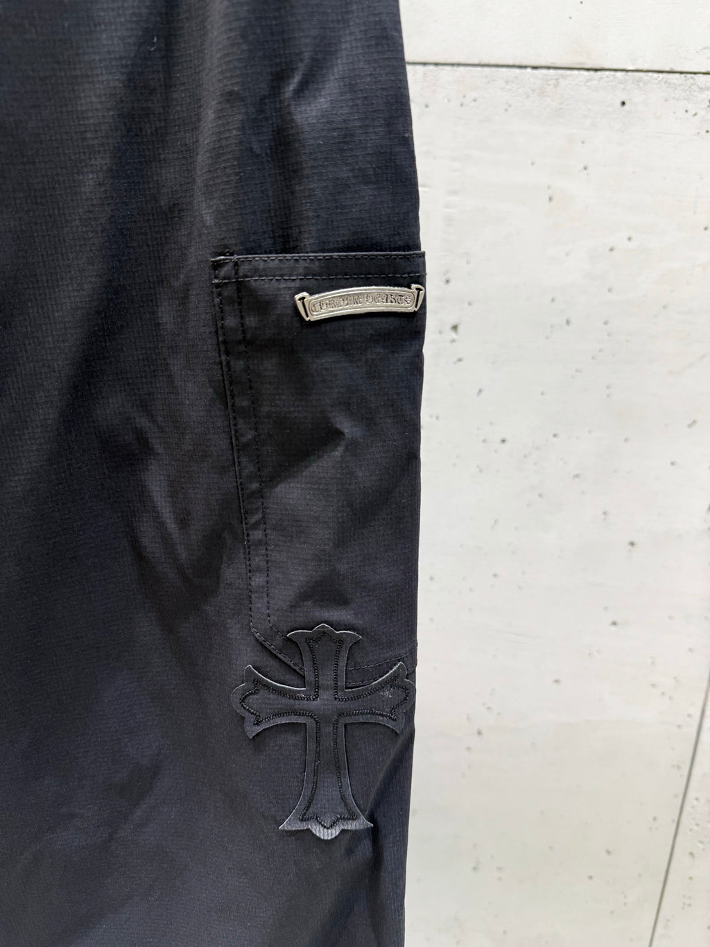 Chrome pants side pocket and raised cross logo patch on dark fabric.