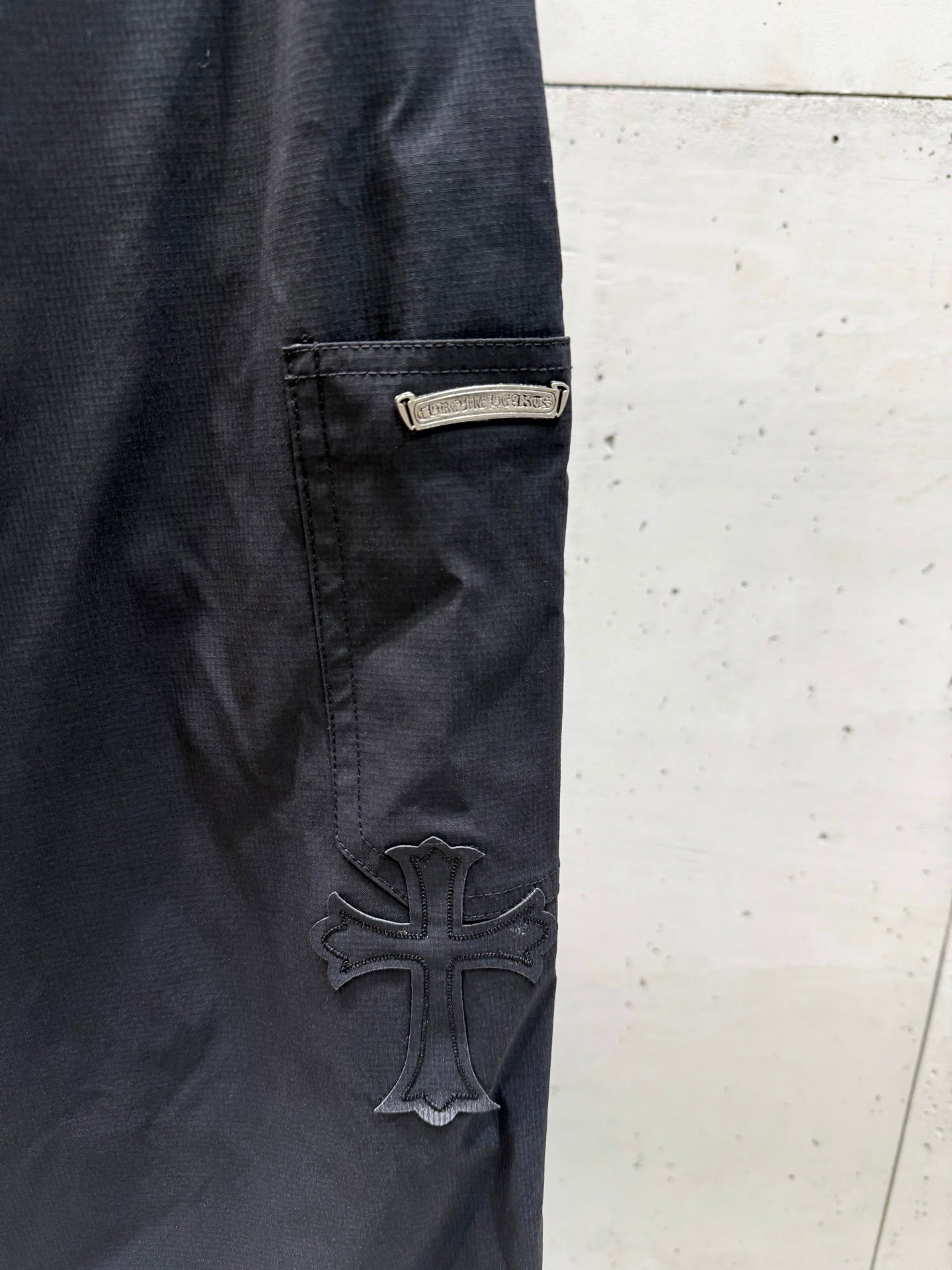 Chrome pants side pocket and raised cross logo patch on dark fabric.