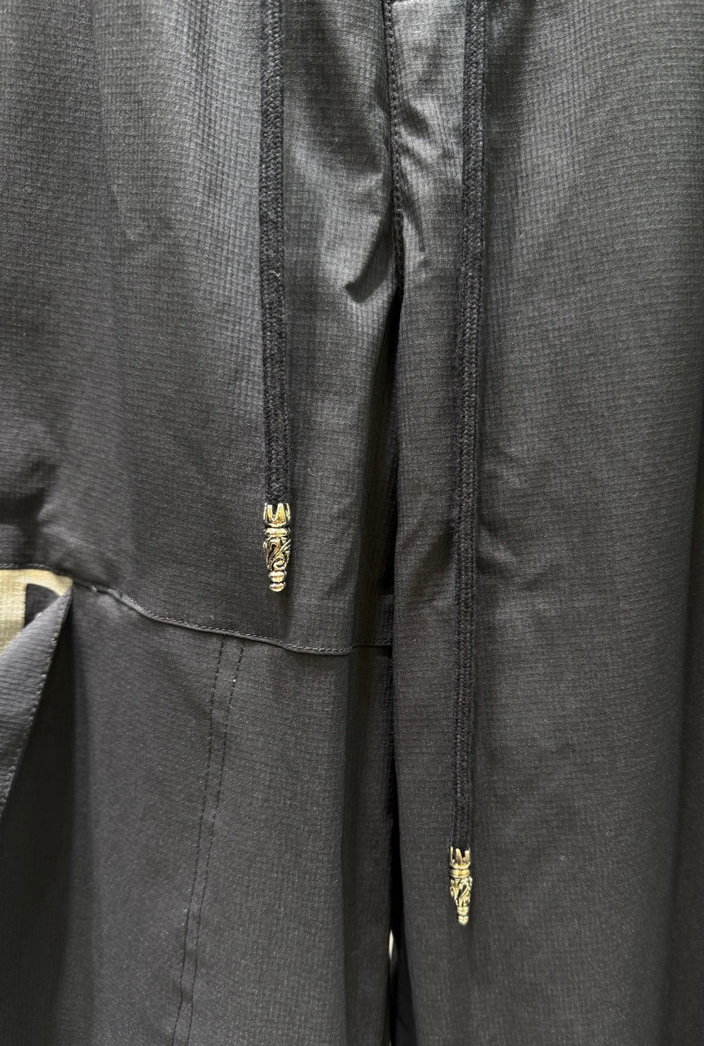 Dark pants with gold zipper fly and small embroidered detail at center seam