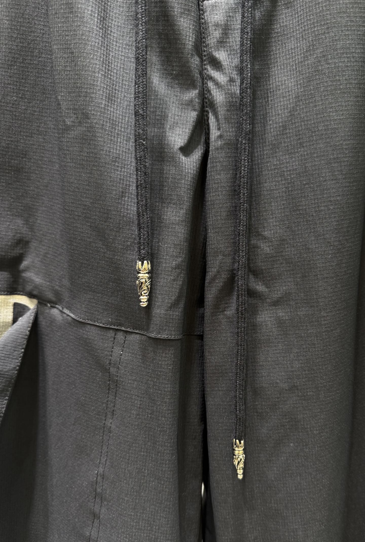 Dark pants with gold zipper fly and small embroidered detail at center seam